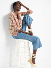 Load image into Gallery viewer, A perfect addition to any outfit ensemble. The Color Weave Knit Jacket stands out with its bold, retro-inspired pattern, crafted from a luxurious, ultra-soft yarn blend. Designed to effortlessly coordinate with the current season's trends, this jacket also boasts a sophisticated woven tape trim and playful pom-pom detailing along the edges, while functional hook-and-eye closures add practicality to its eye-catching design.