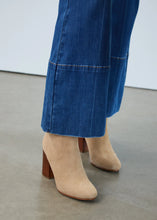 Load image into Gallery viewer, Close-up of bootcut jean and tan suede boot against a white wall.