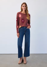 Load image into Gallery viewer, Woman wearing a burgundy sweater with floral patterns, dark indigo jeans and tan suede boots against a white background.