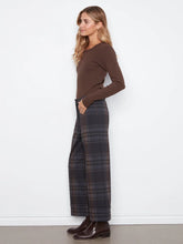 Load image into Gallery viewer, A woman stands in profile wearing a fitted brown long-sleeve top, wide-leg plaid trousers in brown, and dark brown leather boots against a plain white wall.