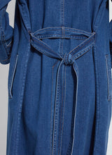 Load image into Gallery viewer, Back of a woman wearing a blue denim trench coat against a white background.