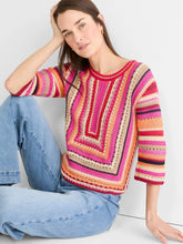 Load image into Gallery viewer, Woman sitting on the ground wearing a red multicolor striped three-quarter sleeve sweater and blue jeans against a light grey background.