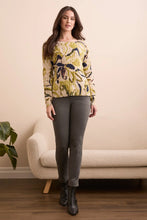 Load image into Gallery viewer, Woman wearing a floral sweater, grey pants and black boots standing in a room with a beige couch and plant.