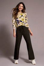 Load image into Gallery viewer, Woman wearing a floral sweater, black pants and white sneakers against a gray background.