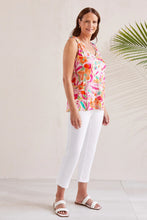 Load image into Gallery viewer, Woman wearing a bright multicolored shoulder tie tank top, white pants and white sandals against a white background with a palm plant.