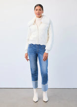Load image into Gallery viewer, Woman wearing a creme textured faux fur jacket, blue jeans with pearl embellished cuffs and white boots against a white wall.