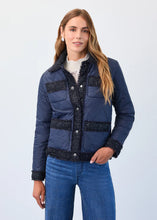 Load image into Gallery viewer, Woman wearing a blue quilted jacket with decorative trim, blue jeans and silver earrings against a light gray background.