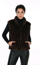 Load image into Gallery viewer, A woman modeling a dark brown faux fur vest with a cheetah print pattern, worn over a black turtleneck and black leather pants, against a plain white background.