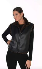 Load image into Gallery viewer, A woman modeling a black faux-leather vest with faux-fur trim and a black long-sleeve top underneath, set against a plain white studio background.