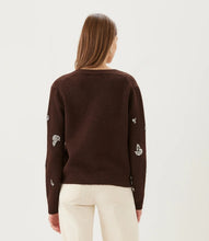 Load image into Gallery viewer, A woman wearing a dark brown knit cardigan with rhinestone floral embroidery and rhinestone drop earrings paired with cream pants, against a plain light gray studio background.