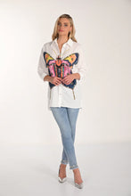 Load image into Gallery viewer, Woman wearing a white blouse with a colorful butterfly design, light blue jeans with embellished hem and silver heels on a white background.