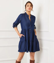 Load image into Gallery viewer, Woman wearing a blue dress and brown knee-high boots against a white paneled wall.