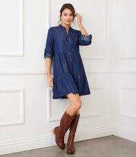 Load image into Gallery viewer, Woman wearing a blue dress and brown knee-high boots against a white paneled wall.
