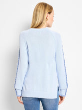 Load image into Gallery viewer, Woman wearing a light blue sweater with a ruffle along the sleeves and blue jeans against a white background.