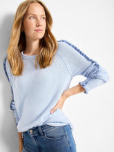 Load image into Gallery viewer, Woman wearing a light blue sweater with a ruffle along the sleeves and blue jeans against a white background.