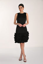 Load image into Gallery viewer, Woman wearing a black dress with a ruffled hem and silver heels on a white background.
