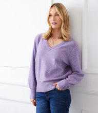 Load image into Gallery viewer, Woman wearing a purple sequin sweater and blue jeans standing against a white wall.