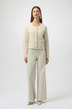 Load image into Gallery viewer, Woman wearing a winter white and gold sequined textured cardigan, winter white pants with gold buttons and off-white heels against a white background.