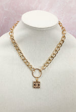 Load image into Gallery viewer, Introducing the extraordinary Shelly necklace! This piece features a rare, gold square adorned with a delicate pearl CC logo. The vintage Chanel button is elegantly suspended from a round connector, attached to a link chain. This exquisite necklace effortlessly complements any outfit. Get ready for endless compliments!