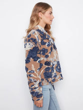 Load image into Gallery viewer, A woman modeling a long-sleeve button-up coat with a camel, navy, and white abstract floral pattern, paired with light-wash blue jeans and black ankle boots, standing against a white wall.