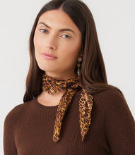 Load image into Gallery viewer, A woman with long dark brown hair models a leopard print neck scarf tied around her collarbone, paired with a brown ribbed knit sweater against a plain light gray background.