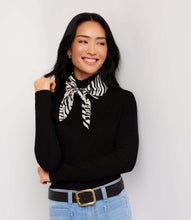 Load image into Gallery viewer, A woman wearing a black ribbed long-sleeve turtleneck sweater with a black and white zebra-print neck scarf tied at the collar, paired with light blue jeans and a black belt with a gold buckle, against a plain light gray background.