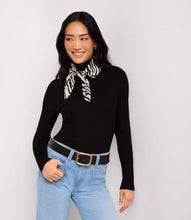 Load image into Gallery viewer, A woman modeling a black ribbed long-sleeve turtleneck sweater with a black and white zebra-print neck scarf, paired with light blue jeans and a black belt, against a light gray studio background.