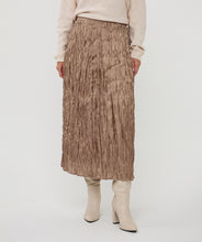 Load image into Gallery viewer, Model wearing a shiny pleated taupe midi skirt, beige sweater and off-white boots against a white background.