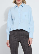 Load image into Gallery viewer, Woman wearing a light blue shirt with embellishments and dark plaid pants against a white background.