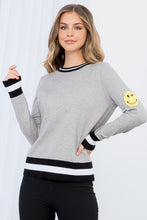 Load image into Gallery viewer, The Heather Gray Smiley Face Knit Sweater - TMK1517 from THML features classic black and white stripes on a gray background but adds a cheerful touch with a darling yellow smiley face on the upper part of each sleeve. This lightweight sweater has a vintage feel and modern appeal, with striping at the bottom hem, cuffs, and neck. Color- Gray, black, white and yellow. Smiley face on upper sleeves. Black and white striping on neckline, sleeves and bottom hem. Lightweight sweater.