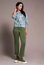 Load image into Gallery viewer, Woman wearing a patterned green, blue, white sweater, green pants and green sneakers against a pale pink background.