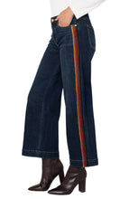 Load image into Gallery viewer, Model wearing dark blue wide leg jean with brown multicolor striping on sides, white long sleeve top and brown boots against a white background.