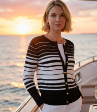 Load image into Gallery viewer, Woman wearing a black and off-white striped cardigan sweater over a white tee and white pants on a boat with a sunset background.