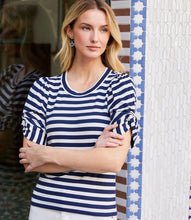 Load image into Gallery viewer, Woman wearing a blue and white striped shirt standing in front of a decorative wall.