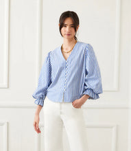 Load image into Gallery viewer, Woman wearing a blue and white striped blouse against a white wall.