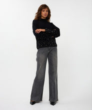 Load image into Gallery viewer, Woman wearing a black sweater with black pearls on lower half of sweater and sleeves, grey pants and black shoes against a white background.