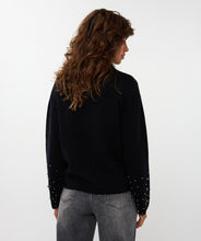 Load image into Gallery viewer, Model wearing a black sweater with black pearls on bottom of sleeves and grey pants against a white background.