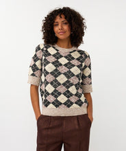 Load image into Gallery viewer, Woman wearing a short sleeve argyle sweater and brown pants against a white wall.