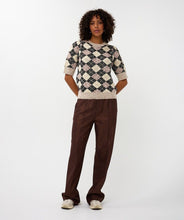 Load image into Gallery viewer, Woman wearing a short sleeve argyle sweater, brown pants and white sneakers against a white background.