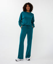 Load image into Gallery viewer, Woman wearing a teal modal sweater with floral embroidery, teal pants and white sneakers against a white background.