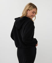 Load image into Gallery viewer, Woman wearing a black hoodie against a white background.