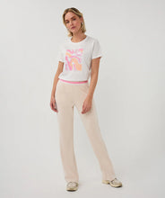 Load image into Gallery viewer, Woman wearing a white t-shirt with pink graphic design, tan pants and sneakers on a plain background.