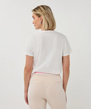 Load image into Gallery viewer, Woman wearing a white t-shirt and tan pants on a plain background.