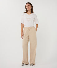 Load image into Gallery viewer, Woman wearing an off-white t-shirt with animal print and tan pants against a white background.
