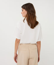 Load image into Gallery viewer, Woman wearing an off-white t-shirt and tan pants against a white background.