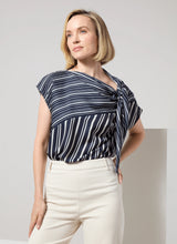 Load image into Gallery viewer, The Tamar Stripe Bow-Tie Neck Top is a standout piece, designed in a nautical collage color with distinctive stripes for a timeless, chic appeal. Made from premium Lightweight Satin, this top offers a luxurious feel while maintaining effortless wearability. Its relaxed, boxy fit is complemented by stylish details like a bow tied to one shoulder and a rounded, high-low shirttail hem. Perfect for casual yet polished ensembles, the Tamar Stripe Bow-Tie Neck Top is a versatile addition.