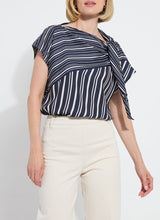 Load image into Gallery viewer, The Tamar Stripe Bow-Tie Neck Top is a standout piece, designed in a nautical collage color with distinctive stripes for a timeless, chic appeal. Made from premium Lightweight Satin, this top offers a luxurious feel while maintaining effortless wearability. Its relaxed, boxy fit is complemented by stylish details like a bow tied to one shoulder and a rounded, high-low shirttail hem. Perfect for casual yet polished ensembles, the Tamar Stripe Bow-Tie Neck Top is a versatile addition.