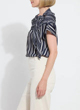 Load image into Gallery viewer, The Tamar Stripe Bow-Tie Neck Top is a standout piece, designed in a nautical collage color with distinctive stripes for a timeless, chic appeal. Made from premium Lightweight Satin, this top offers a luxurious feel while maintaining effortless wearability. Its relaxed, boxy fit is complemented by stylish details like a bow tied to one shoulder and a rounded, high-low shirttail hem. Perfect for casual yet polished ensembles, the Tamar Stripe Bow-Tie Neck Top is a versatile addition.