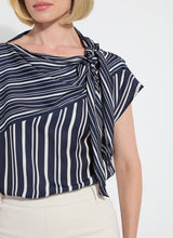 Load image into Gallery viewer, The Tamar Stripe Bow-Tie Neck Top is a standout piece, designed in a nautical collage color with distinctive stripes for a timeless, chic appeal. Made from premium Lightweight Satin, this top offers a luxurious feel while maintaining effortless wearability. Its relaxed, boxy fit is complemented by stylish details like a bow tied to one shoulder and a rounded, high-low shirttail hem. Perfect for casual yet polished ensembles, the Tamar Stripe Bow-Tie Neck Top is a versatile addition.