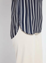 Load image into Gallery viewer, The Tamar Stripe Bow-Tie Neck Top is a standout piece, designed in a nautical collage color with distinctive stripes for a timeless, chic appeal. Made from premium Lightweight Satin, this top offers a luxurious feel while maintaining effortless wearability. Its relaxed, boxy fit is complemented by stylish details like a bow tied to one shoulder and a rounded, high-low shirttail hem. Perfect for casual yet polished ensembles, the Tamar Stripe Bow-Tie Neck Top is a versatile addition.